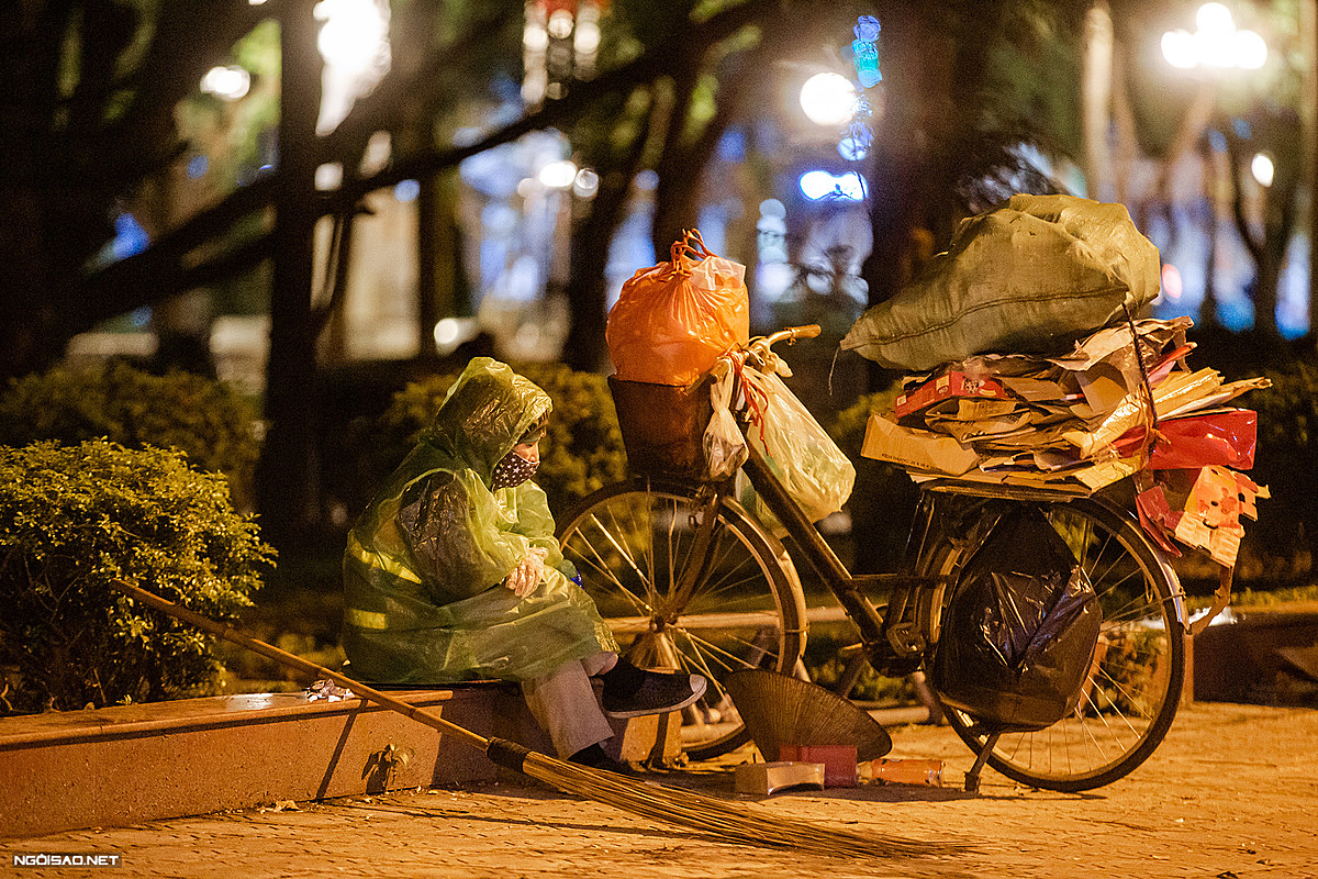 A scrap dealer huddles against the cold as she takes a break on the sidewalk of Thuy Khue Street in Tay Ho District.