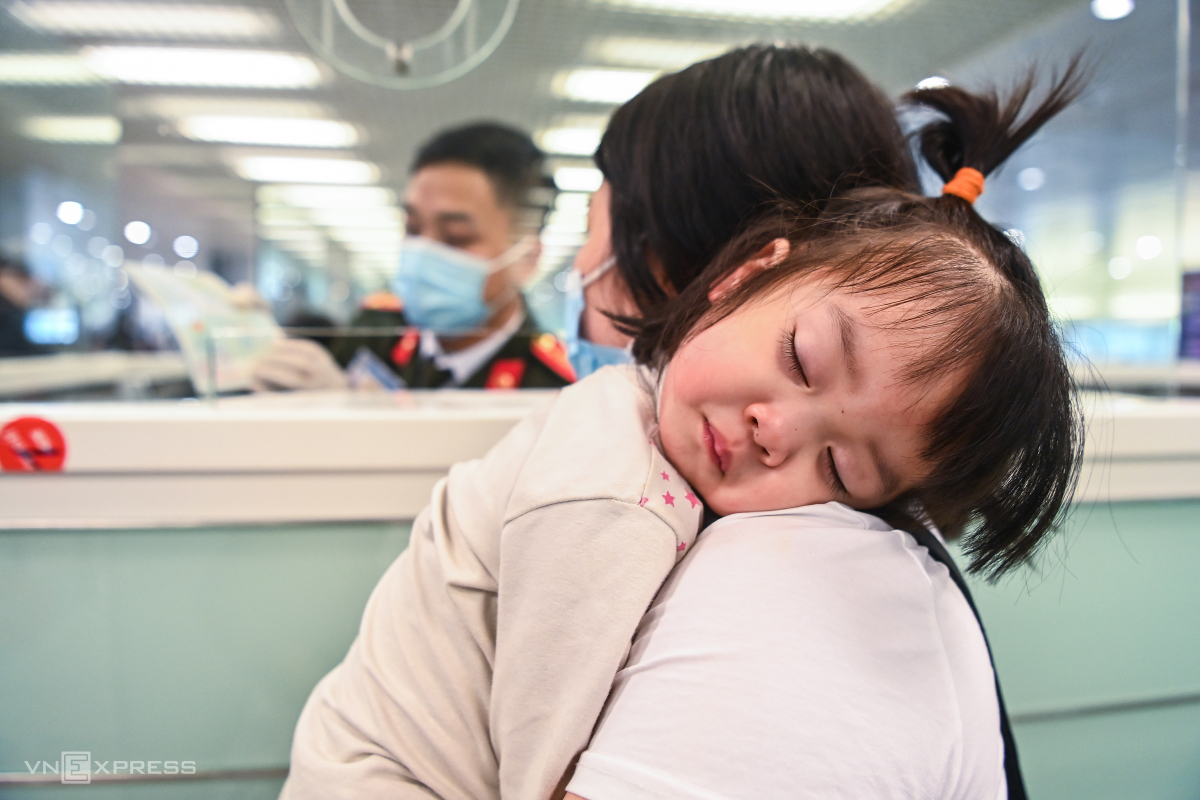 A kid is tired after a long flight, laying down on her mothers shoulder during immigration procedures.