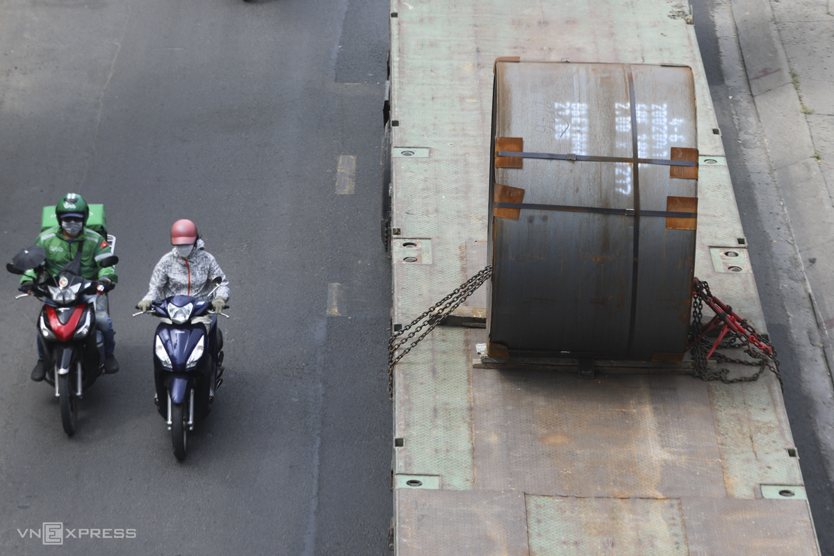 Motorcyclists drive right beside a trailer carrying steel coils on Huynh Tan Phat Street.