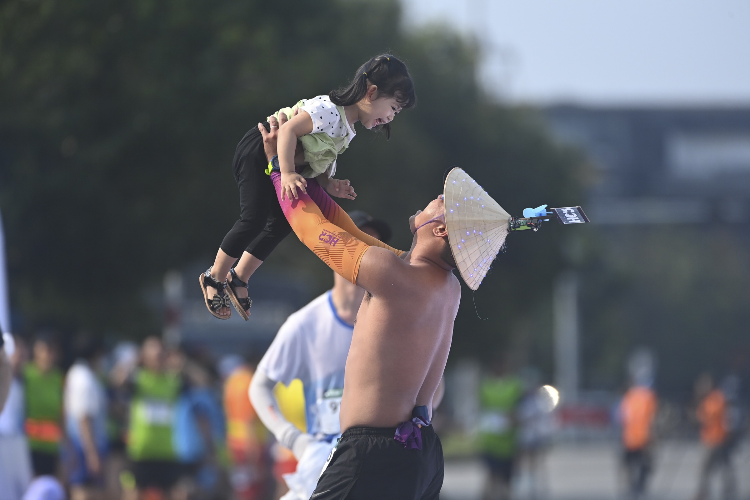 Wearing the Vietnamese conical hat non la, a runner lifts his daughter in celebration.
